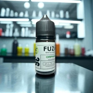 A small bottle with a black cap labeled 'FUZION throwback ORPHAN strawberry' placed on a reflective surface, with blurred background items featuring various colored bottles.